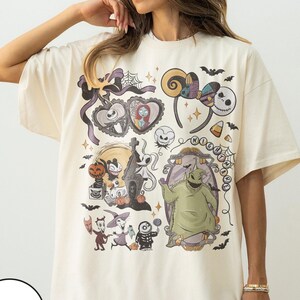 May include: Ivory-colored t-shirt featuring a collage of characters and elements from "The Nightmare Before Christmas." The design includes Jack Skellington, Sally, Oogie Boogie, and other iconic imagery. The shirt has a relaxed fit.