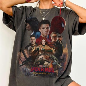 May include: Dark gray t-shirt featuring a movie poster design with multiple characters, including Spider-Man. The text "SPIDER-MAN BRAND NEW DAY" is prominently displayed. The shirt has a vintage, worn look.