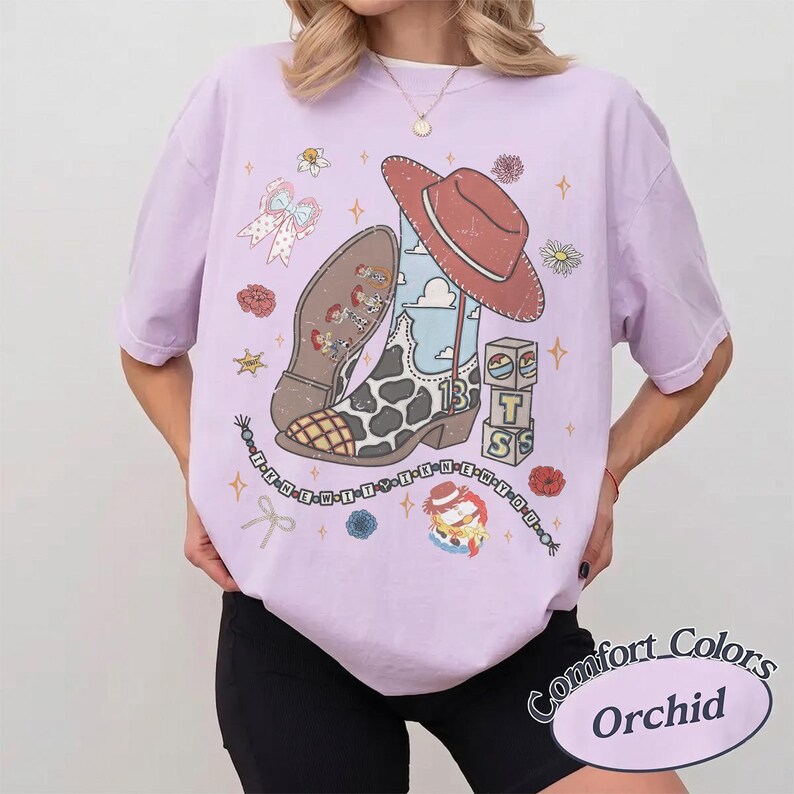 May include: A light purple t-shirt featuring a graphic print of a cowboy boot with a cow print pattern, a red hat, building blocks with the letters T, S, and a cloud design, a bow, flowers, and a string of beads with the text I-K-N-E-W-T-T-Y-N-E-W-Y-O-U.