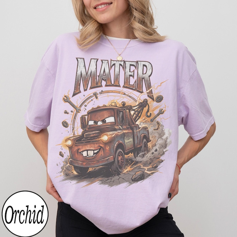 K&ouml;nnte beinhalten: Helllila T-Shirt mit einem Cartoon-Bild von Hook aus dem Film Cars. Das Wort "MATER" ist in einer verwitterten Schriftart &uuml;ber dem Bild aufgedruckt. Das Bild enth&auml;lt Schraubenschl&uuml;ssel und ein kreisf&ouml;rmiges Design.