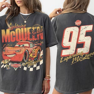 May include: Dark gray Lightning McQueen t-shirt featuring a graphic of the character and the number 95. The front design includes the text "Lightning McQueen" and "Cars". The back of the shirt displays the number 95 and "Lightning McQueen".
