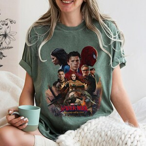 May include: Green t-shirt featuring a graphic of characters from the Spider-Man movie. The design includes images of actors and the text "Spider-Man: Brand New Day". The shirt is a comfortable, casual style.
