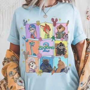 Puede incluir: Camiseta azul claro con un gr&aacute;fico colorido de personajes de la pel&iacute;cula animada "Zootr&oacute;polis". El dise&ntilde;o incluye a Judy Hopps, Nick Wilde y otros personajes en una cuadr&iacute;cula. La palabra "Zootr&oacute;polis" tambi&eacute;n es visible.