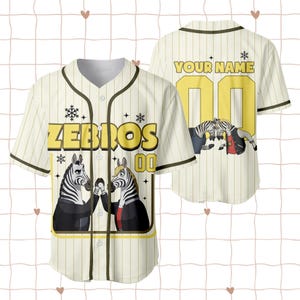 Puede incluir: Camiseta de b&eacute;isbol color crema con rayas verticales y cierre de botones. La camiseta presenta la palabra "ZEBROS" en letras amarillas, junto con un gr&aacute;fico de dos cebras. Tambi&eacute;n se muestra el n&uacute;mero "00".