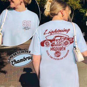 May include: Light blue t-shirt with a graphic of Lightning McQueen and the number 95. The front of the shirt has a small graphic with the number 95 and the text "Lightning McQueen". The back of the shirt features a larger design.