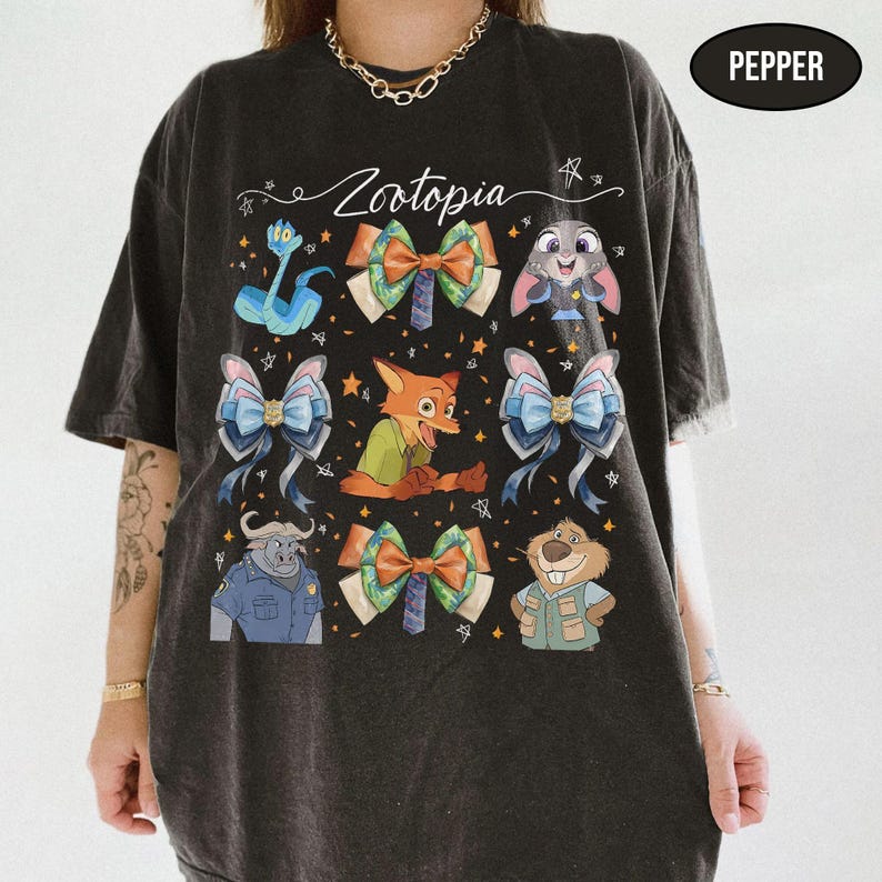 May include: A black short-sleeve t-shirt featuring a graphic print with the text Zootopia, various character illustrations including a fox, rabbit, and buffalo, and several decorative bows interspersed with small star shapes. The shirt colour is Pepper.