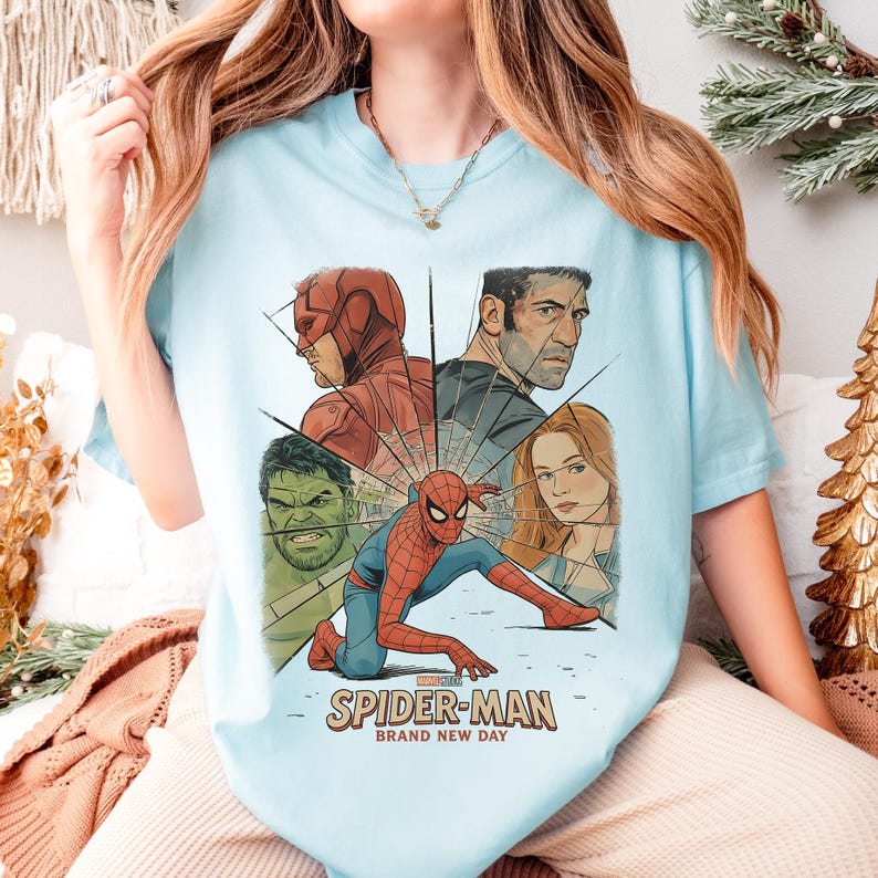 May include: Light blue t-shirt featuring a graphic of Spider-Man and other Marvel characters. The design includes Daredevil, Hulk, and The Punisher. The text "SPIDER-MAN BRAND NEW DAY" is printed below the characters.