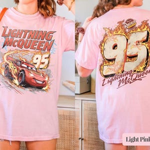 May include: Pale pink t-shirt with a graphic of Lightning McQueen and the number 95 from the Cars film. The front shows Lightning McQueen racing with flames. The back has the number 95 in flames and "Lightning McQueen".