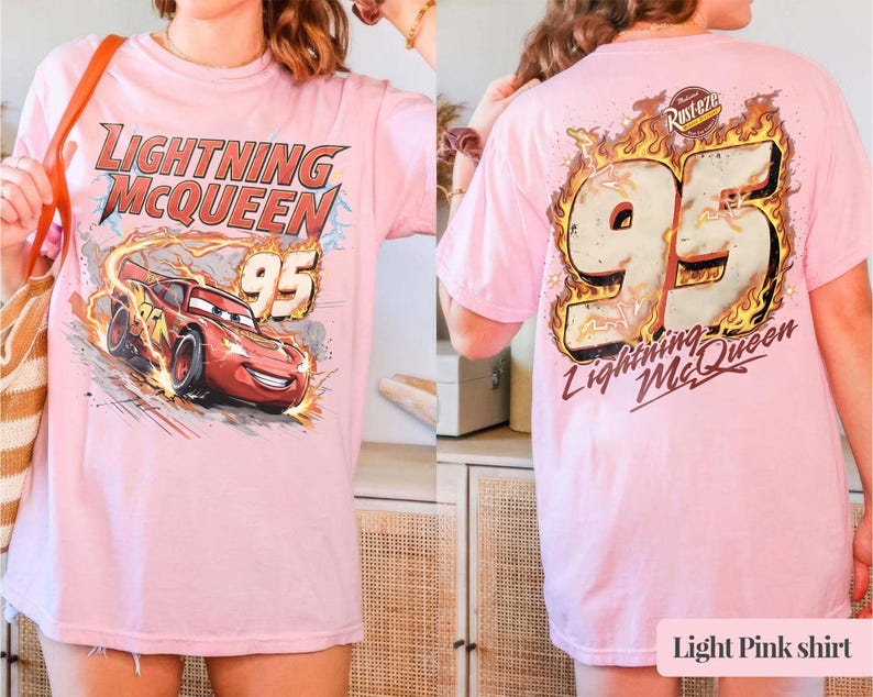May include: Pale pink t-shirt with a graphic of Lightning McQueen and the number 95 from the Cars film. The front shows Lightning McQueen racing with flames. The back has the number 95 in flames and "Lightning McQueen".