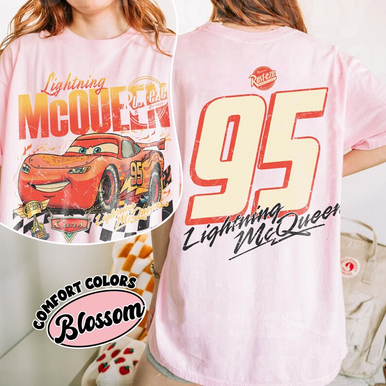 May include: A light pink t-shirt featuring Lightning McQueen from the Cars movie. The front graphic shows the car with the text "Lightning McQueen" and "95". The back of the shirt displays a large "95" and "Lightning McQueen".