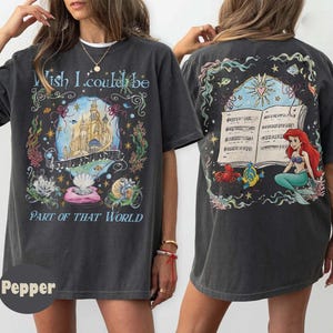 May include: Dark gray t-shirt with a colorful graphic featuring a castle, musical notes, and the text "Wish I could be Part of That World" on the front. The back of the shirt has a graphic of a mermaid and musical notes.