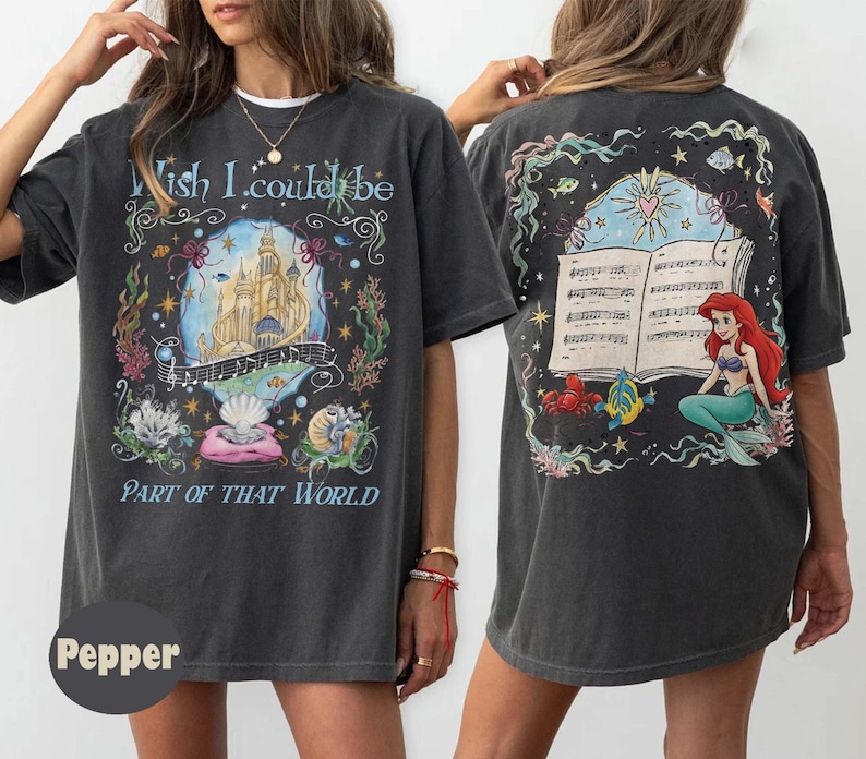 May include: Dark gray t-shirt with a colorful graphic featuring a castle, musical notes, and the text "Wish I could be Part of That World" on the front. The back of the shirt has a graphic of a mermaid and musical notes.