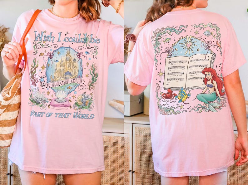 May include: Pink t-shirt featuring a colorful illustration from "The Little Mermaid." The front design includes a castle, musical notes, and text that reads "Wish I could be part of that world." The back shows Ariel, a crab, and a fish.