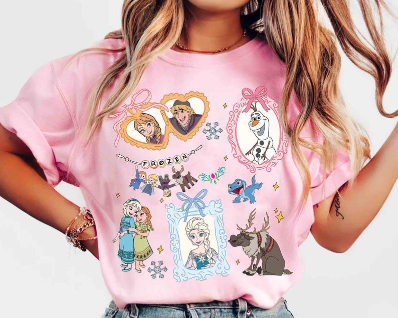 以下が含まれることがあります： アニメ映画「アナと雪の女王」のキャラクターが複数フレームに収められたピンク色のTシャツ。フレームにはアナ、エルサ、オラフ、クリストフ、スヴェンが含まれています。「FROZEN」の文字が装飾的なフォントで上部に表示されています。