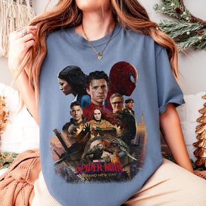 May include: A light blue t-shirt featuring a graphic from the movie Spider-Man: Brand New Day. The graphic includes several characters from the film, including Spider-Man, and the text "Spider-Man Brand New Day".