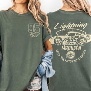 May include: Olive green t-shirt featuring the number 95 and the words "Lightning McQueen" on the front. The back of the shirt displays a graphic of a race car with the text "Lightning McQueen" and "Seven Time Piston Cup Champion".