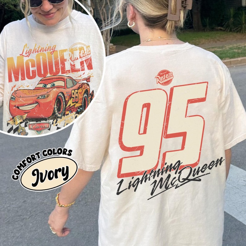 May include: Ivory-colored t-shirt featuring Lightning McQueen graphics. The front displays the character and text, while the back showcases a large "95" and the Lightning McQueen logo. The shirt is part of the Comfort Colors collection.