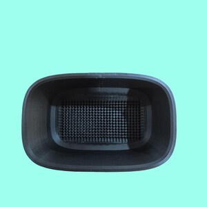 May include: A black, rectangular container with rounded corners and a perforated interior base. The container is set against a light teal background. The design suggests a functional, possibly 3D-printed, item.