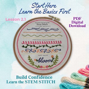 May include: A wooden embroidery hoop containing white fabric with various embroidered lines, curves, and the word bloom in blue thread. Text on the fabric includes Start Here Learn the Basics First, Lesson 2.1, PDF Digital Download, and Build Confidence Learn the STEM STITCH. Colourful embroidery floss skeins are visible.