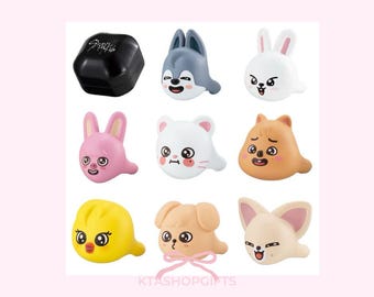 May include: A collection of nine colorful, cartoon animal figurines, including a black box with white text, a gray wolf, a white rabbit, a pink rabbit, a white cat, a brown dog, a yellow chick, a tan dog with a pink bow, and a cream-colored fox.
