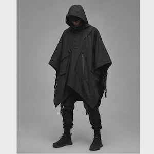 May include: A black hooded poncho featuring a high collar, a vertical zippered chest pocket, and multiple adjustable straps with buckles along the sides. The garment is paired with matching black tapered trousers and black athletic sneakers.