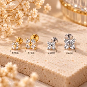 May include: Four flower-shaped stud earrings with clear round stones and a central bead. Two are gold-toned and two are silver-toned, with sizes labeled as 2.9mm and 3.7mm. Each earring features a flat back post for secure placement in piercings.