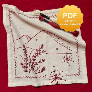 May include: Cream-colored embroidered fabric with a winter landscape design. The design features mountains, snowflakes, and foliage in a deep red thread. The fabric is bordered with a matching red stitch. The image includes the text "PDF pattern + video tutorial".