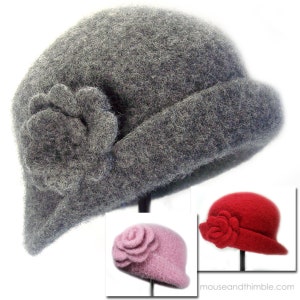 May include: Three felt hats with flower embellishments. The hats are grey, pink, and red. The hats are on display against a white background.