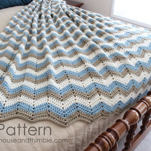 May include: A crocheted chevron blanket in shades of blue, brown, and white. The blanket is draped over a bed with a wooden headboard.