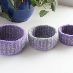 May include: Three felted wool bowls in different sizes. The bowls are purple and gray with a speckled pattern.