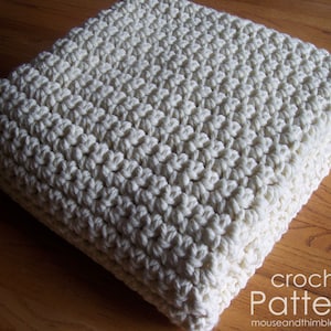 May include: A white crocheted blanket with a textured stitch pattern. The blanket is folded in half and lying on a wooden surface. The text "crochet pattern" is visible in the lower right corner of the image.
