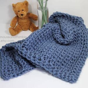 May include: A soft, blue crocheted baby blanket with a textured stitch pattern. The blanket is folded and draped over a white surface.