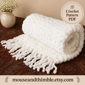 May include: A white crocheted blanket with a thick, textured stitch and long fringe along the edge. A circular badge in the upper right corner reads Crochet Pattern PDF. The text mouseandthimble.etsy.com is printed at the bottom.