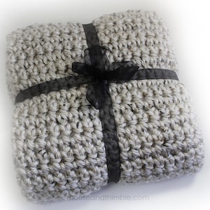 May include: A gray crocheted blanket tied with a black ribbon. The blanket is made with a chunky yarn and has a textured look.