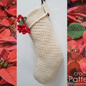 Op de afbeelding: Een gehaakte kerstsok in crèmekleur met een houten kraal aan de bovenkant. De sok hangt aan een witte muur met rode kerststerren aan beide kanten.