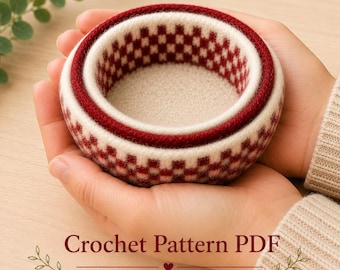 May include: A small, round, felted bowl featuring a cream and deep red checkered pattern. The bowl has a thick, textured rim and a solid cream-colored interior base. The text "Crochet Pattern PDF" and "mouseandthimble.etsy.com" appear below.