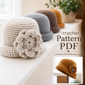 May include: A row of four crocheted hats in cream, gray, brown, and mustard yellow, each featuring a large crocheted flower on the side. The text reads crochet Pattern PDF mouseandthimble.etsy.com, with an inset showing a mustard hat with a button.