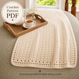 May include: A cream-colored crochet blanket with a textured stitch pattern and a simple border. A wooden tray holds a white teapot, a matching teacup with tea, and a small glass vase with white flowers. Text reads Crochet Pattern PDF.