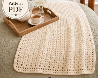 May include: A cream-colored crochet blanket with a textured stitch pattern and a simple border. A wooden tray holds a white teapot, a matching teacup with tea, and a small glass vase with white flowers. Text reads Crochet Pattern PDF.