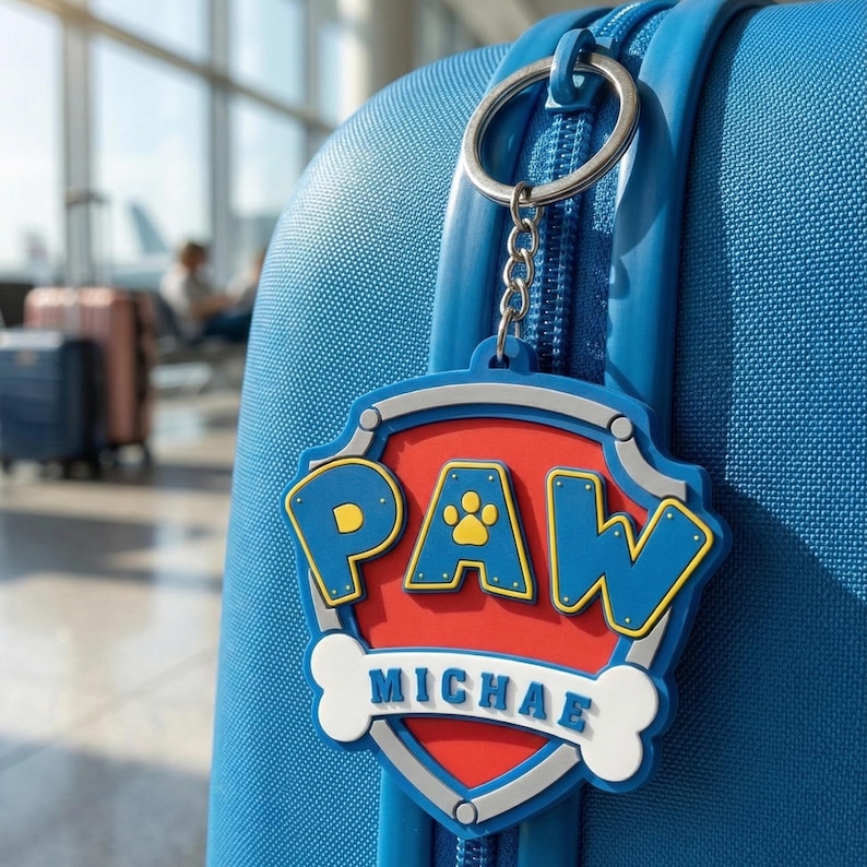 May include: A blue luggage tag with the word "PAW" in blue and yellow letters, a red background, and the name "MICHAEL" below. The tag is attached to a blue suitcase with a silver keyring.