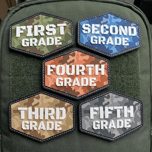 May include: Five hexagonal patches with white block lettering. The top left patch is green camouflage with 'FIRST GRADE', the top right is blue camouflage with 'SECOND GRADE', the center is orange camouflage with 'FOURTH GRADE', the bottom left is tan camouflage with 'THIRD GRADE', and the bottom right is gray camouflage with 'FIFTH GRADE'.