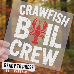 May include: A clear DTF transfer sheet featuring the white distressed text CRAWFISH BOIL CREW with a red crawfish illustration replacing the letter O. The text READY TO PRESS DTF TRANSFER is printed on a separate white label at the bottom.