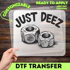 May include: A clear DTF transfer sheet featuring a black graphic of two metal hex nuts and the text JUST DEEZ in a bold, arched font. The design is printed on a transparent film, showcasing the detailed shading and texture of the hardware components.