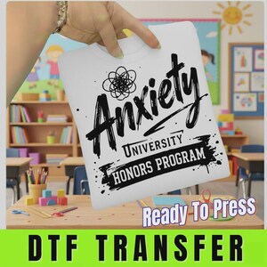 May include: A white DTF transfer sheet featuring black graphic text that reads Anxiety UNIVERSITY HONORS PROGRAM with a scribbled circular icon above the word Anxiety. The design is printed on a smooth, rectangular surface ready for heat application.