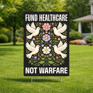 May include: A black yard sign with the text "FUND HEALTHCARE NOT WARFARE" in white. The sign features four white doves with floral and leaf designs in pink, purple, and orange. The sign is displayed on a green lawn.