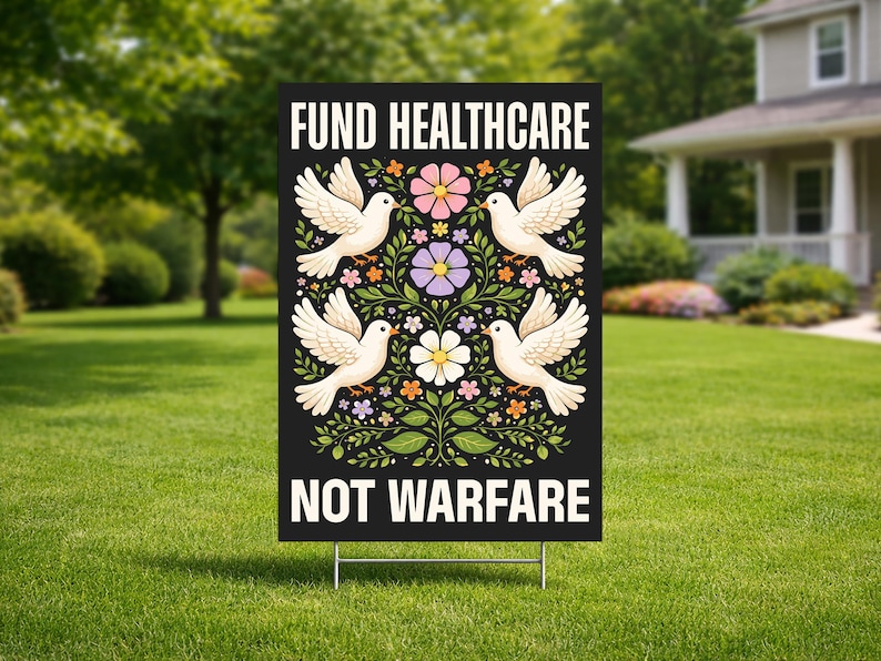 May include: A black yard sign with the text "FUND HEALTHCARE NOT WARFARE" in white. The sign features four white doves with floral and leaf designs in pink, purple, and orange. The sign is displayed on a green lawn.