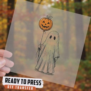 May include: A DTF transfer sheet featuring a graphic illustration of a ghost draped in a white sheet, holding a string attached to an orange jack-o'-lantern balloon. The text READY TO PRESS DTF TRANSFER is printed at the bottom of the sheet.