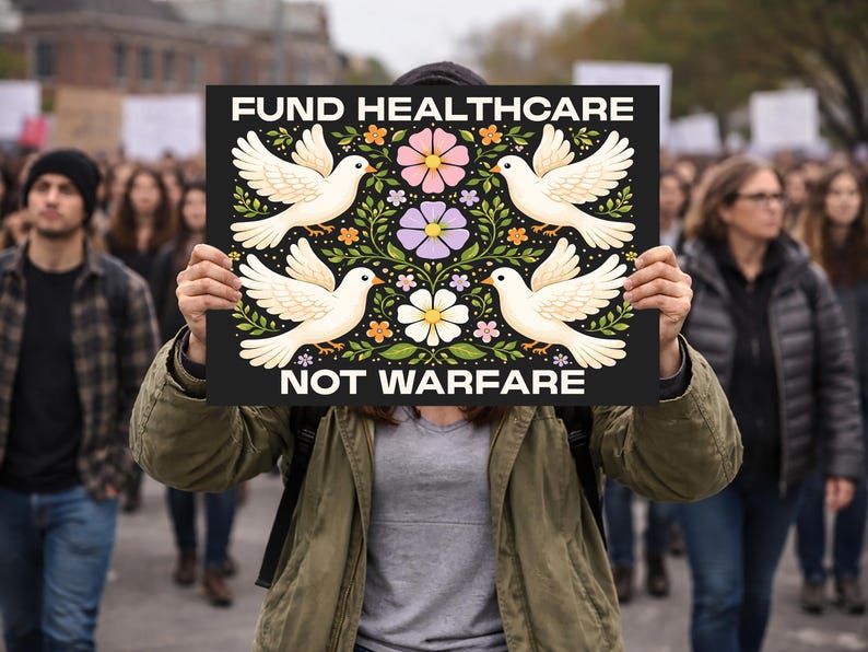 May include: A black sign with the words "FUND HEALTHCARE NOT WARFARE" in white. The sign features four white doves with floral and leaf designs in pink, purple, and yellow. The sign is held up in a crowd of people.