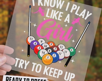 May include: A transparent DTF transfer sheet featuring a graphic of billiard balls numbered 1 through 15 arranged in a triangle, flanked by two pool cues. The text reads I KNOW I PLAY LIKE A GIRL TRY TO KEEP UP in white and pink lettering.
