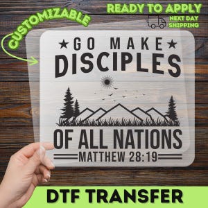 May include: A clear DTF transfer sheet featuring a black graphic design with the text GO MAKE DISCIPLES OF ALL NATIONS MATTHEW 28:19. The design includes a sun, birds, pine trees, and mountain silhouettes centered between the lines of text.